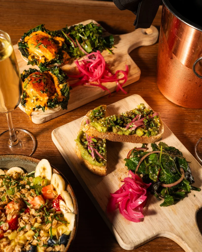 Hummus and beet toasts on a wood board beside a copper cup and sparkling wine