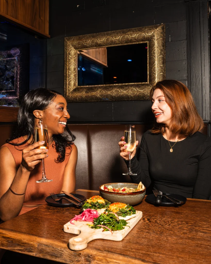 Two guests toasting with sparkling wine in a dark leather booth