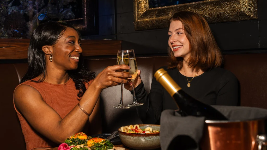 Two friends laughing over brunch in a leather booth