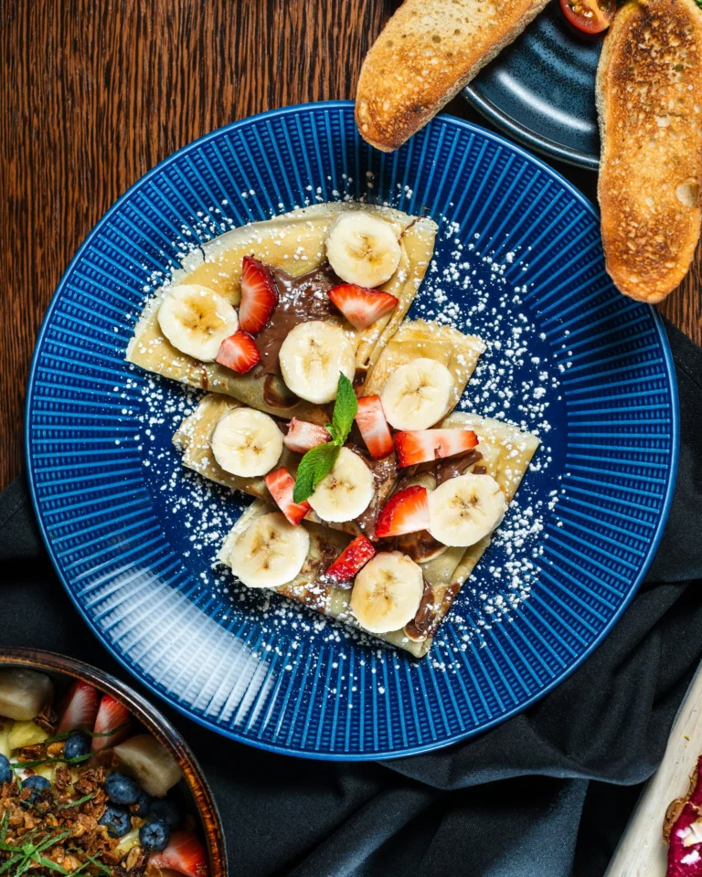 Folded crepes with banana, strawberry, chocolate and powdered sugar on a blue plate
