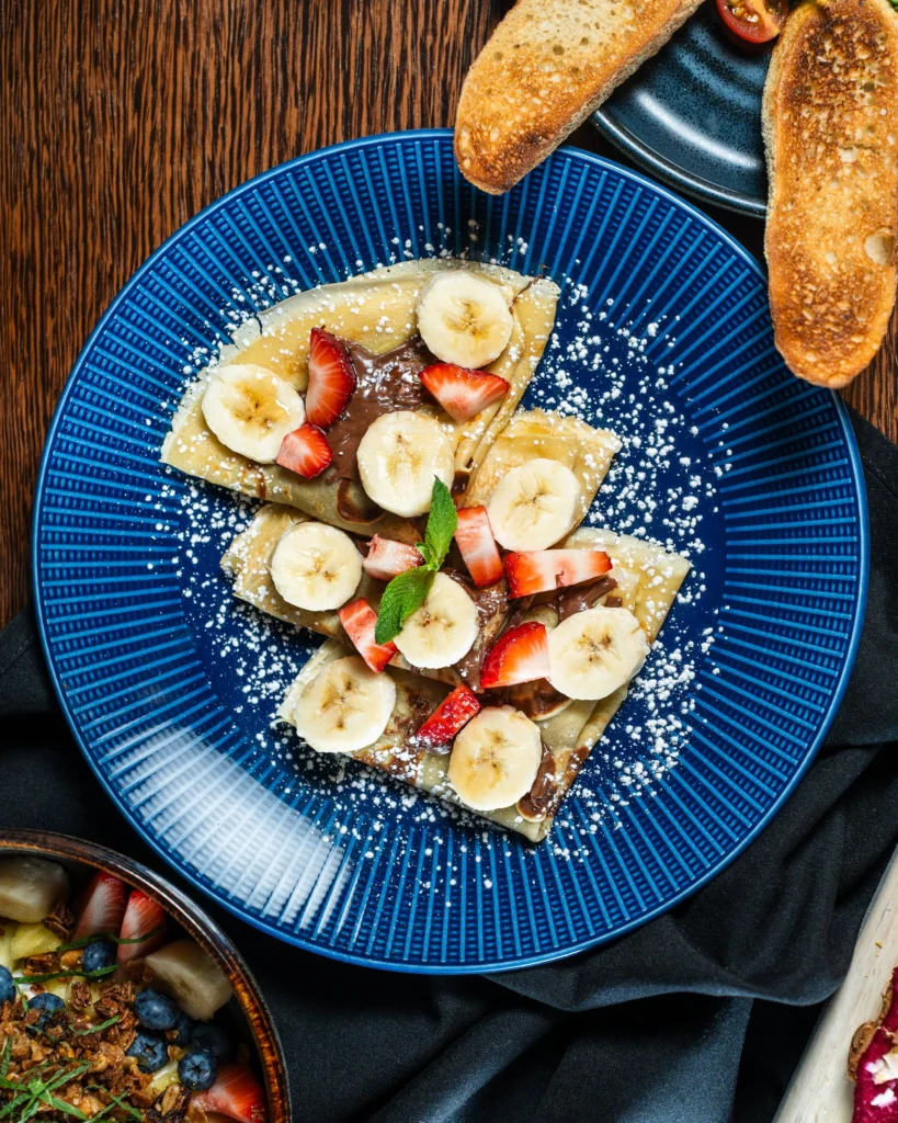 Folded crepes with banana, strawberry, chocolate and powdered sugar on a blue plate