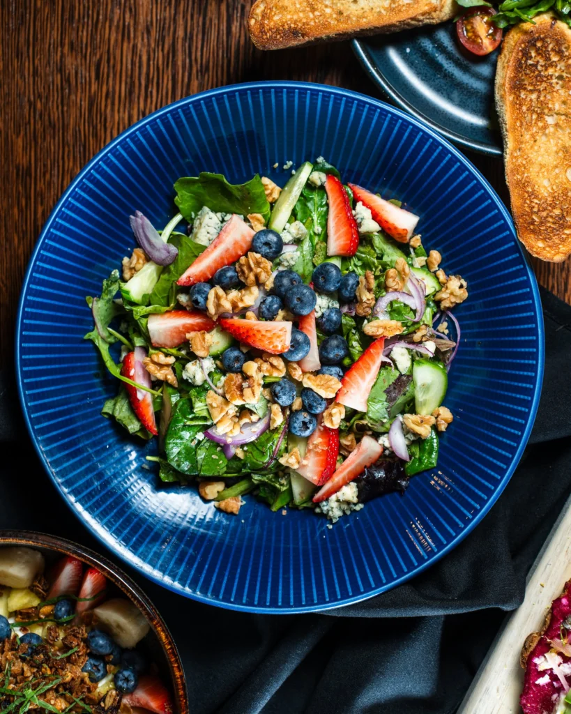 Spring greens with strawberries, blueberries, walnuts, cucumber and blue cheese on a blue plate