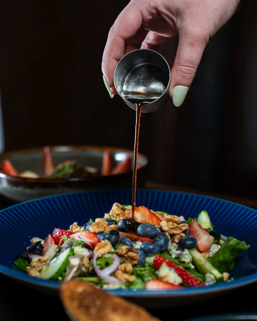 Balsamic being poured from a steel cup over a berry and walnut salad