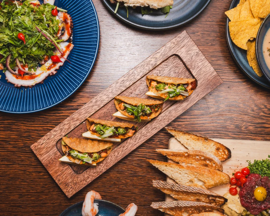 Poke tacos on a wooden board with toasted bread and shrimp cocktail