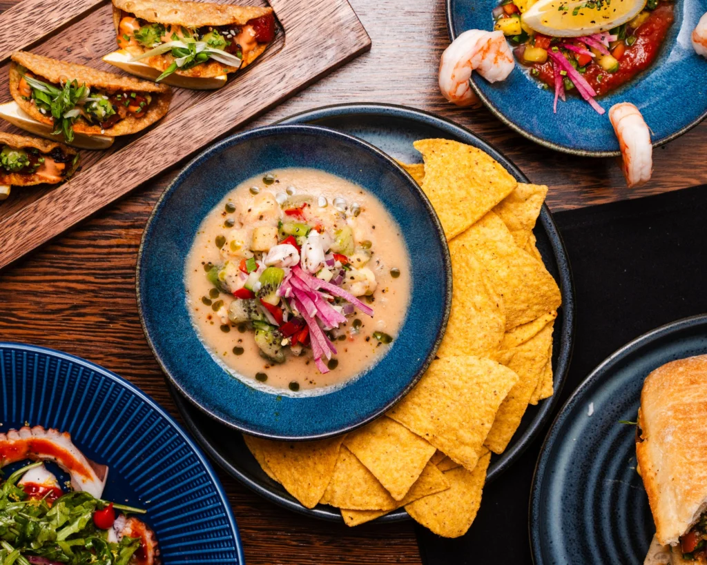 Ceviche with kiwi, pickled onion and herb oil in a blue bowl with tortilla chips