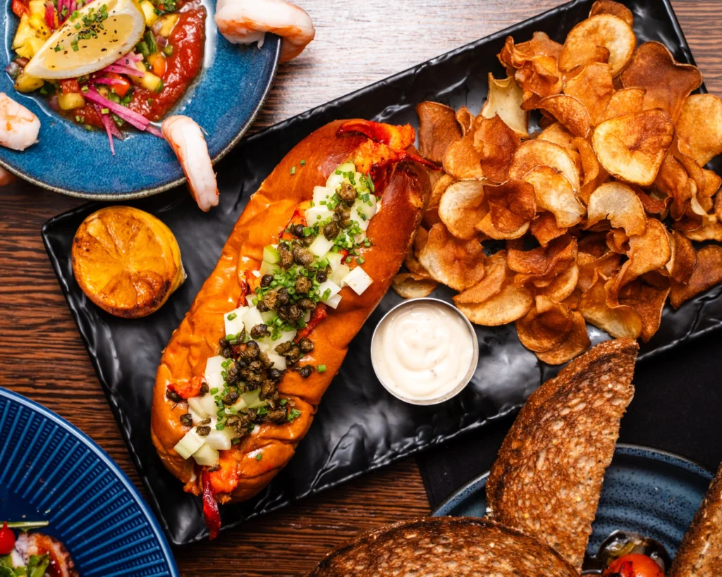 Lobster roll on a brioche bun with fried capers, house chips and a charred lemon