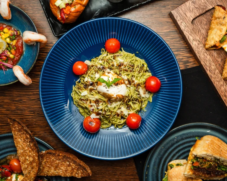 Angel hair pesto pasta with burrata and blistered cherry tomatoes on a blue plate