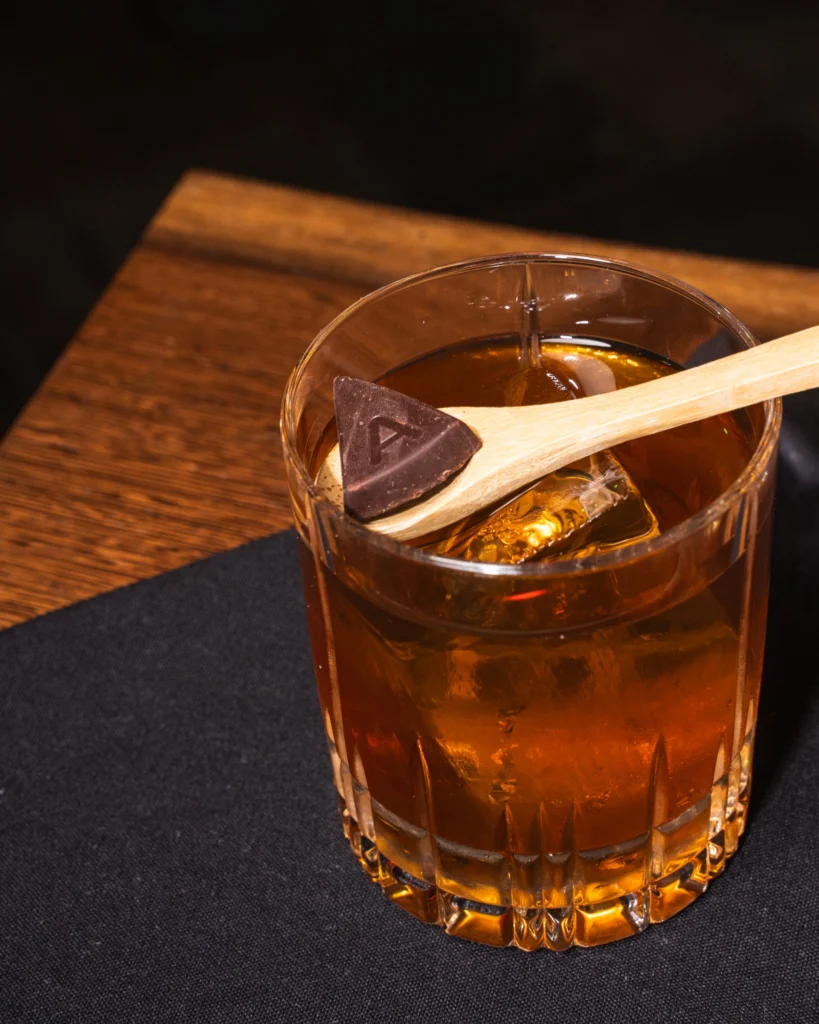 Rocks glass cocktail with a cinnamon stick on a dark napkin