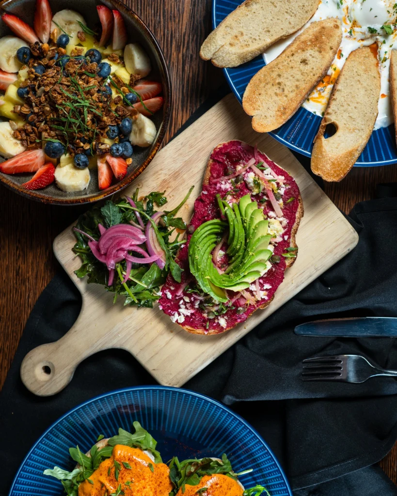 Beet hummus and avocado toast on a wooden board with pickled onion greens