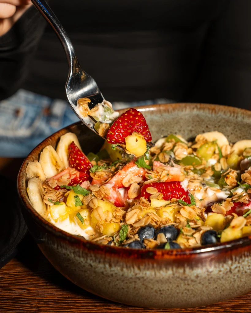 A spoon lifting granola and strawberries from a yogurt bowl
